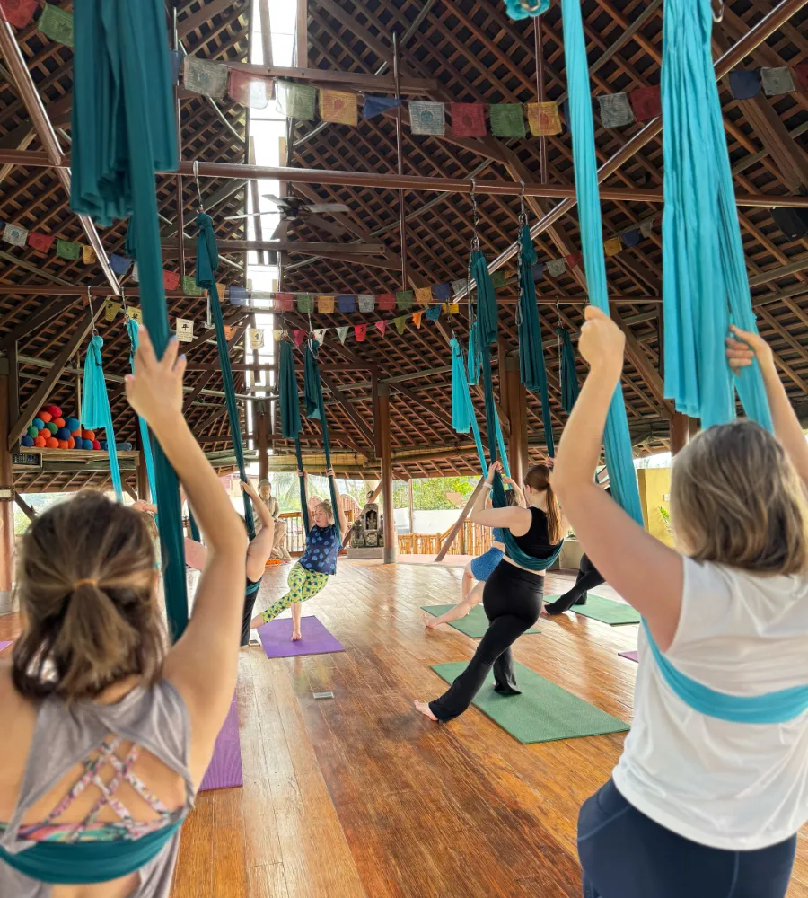 A group of people practicing aerial yoga in a bamboo yoga shala in Bali.